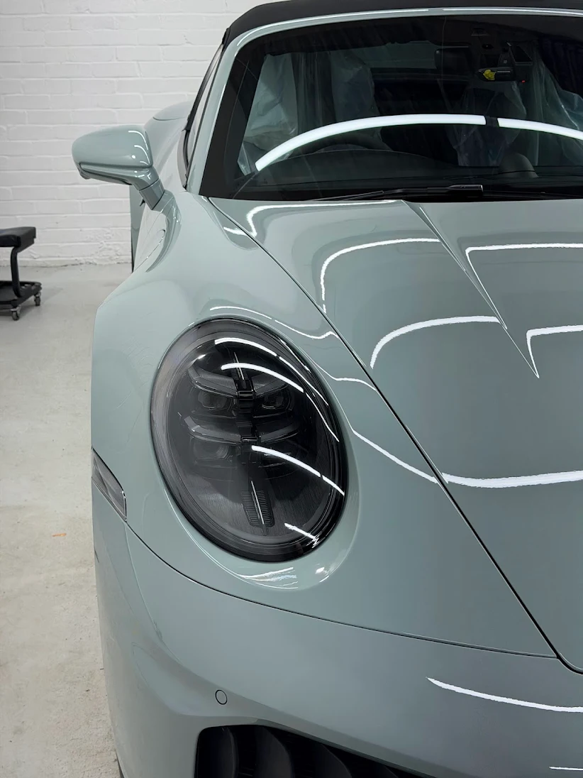 Close detail of a protected headlight and front wing under studio inspection lighting, RainCity PPF